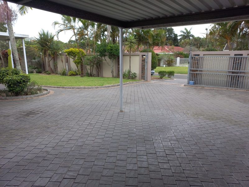 A paved driveway area featuring a covered carport structure, perimeter walling, and a sliding metal gate providing access to the property.