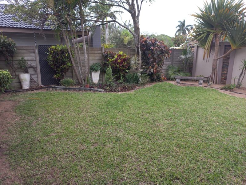 A well-maintained private rear garden featuring a manicured lawn, established perimeter landscaping, and a secure boundary wall.