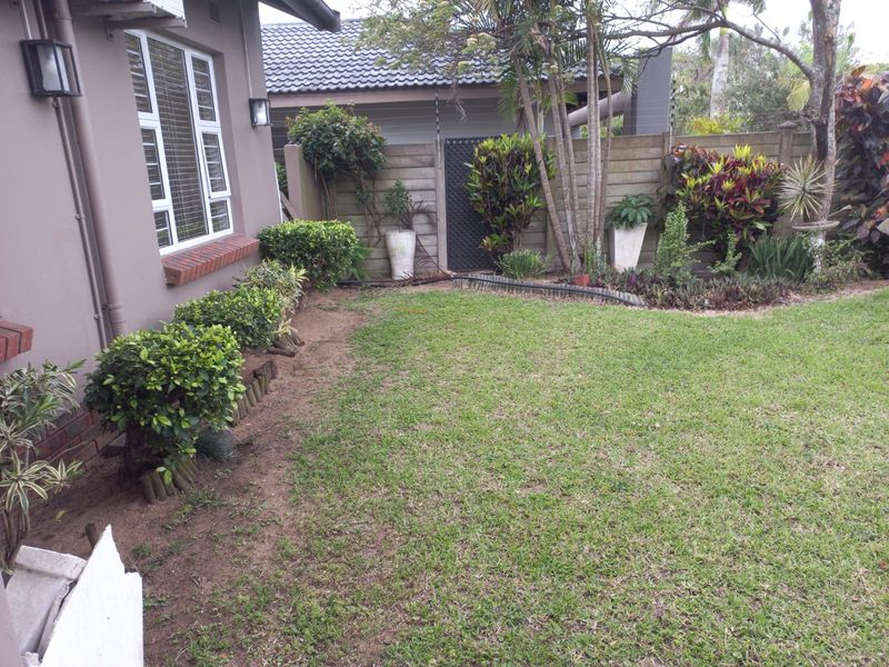 A private rear garden area featuring a well-maintained lawn, established perimeter landscaping, and a secure boundary wall.