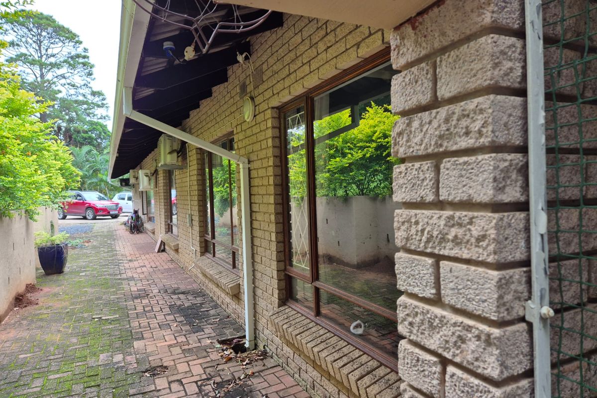 Exterior view of the side of the house featuring brick facade, large windows, and a paved walkway showing signs of wear and maintenance needs.