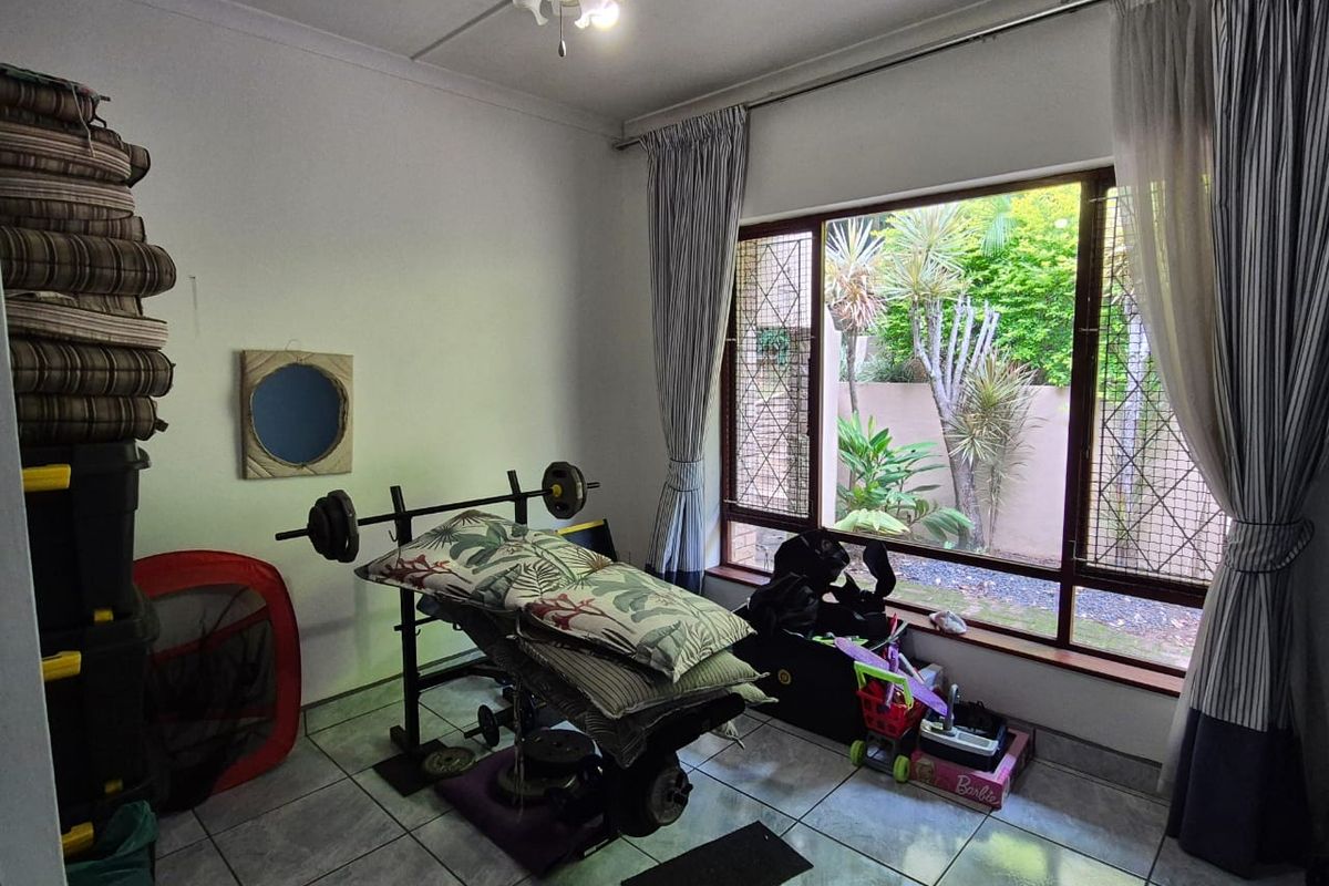 A bedroom featuring tiled flooring and a large window with security bars, overlooking a private garden area.