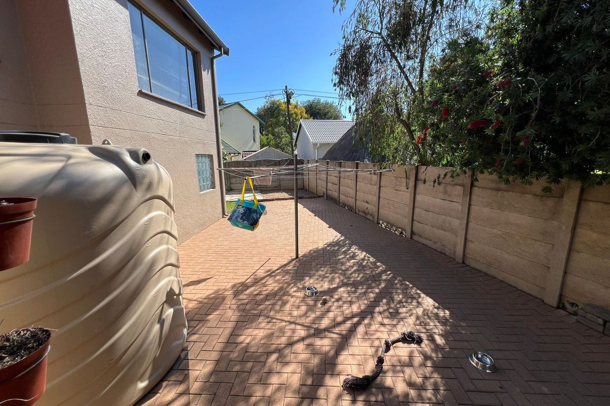 A paved rear courtyard area featuring a precast concrete boundary wall, a rotary clothesline, and a large water storage tank.