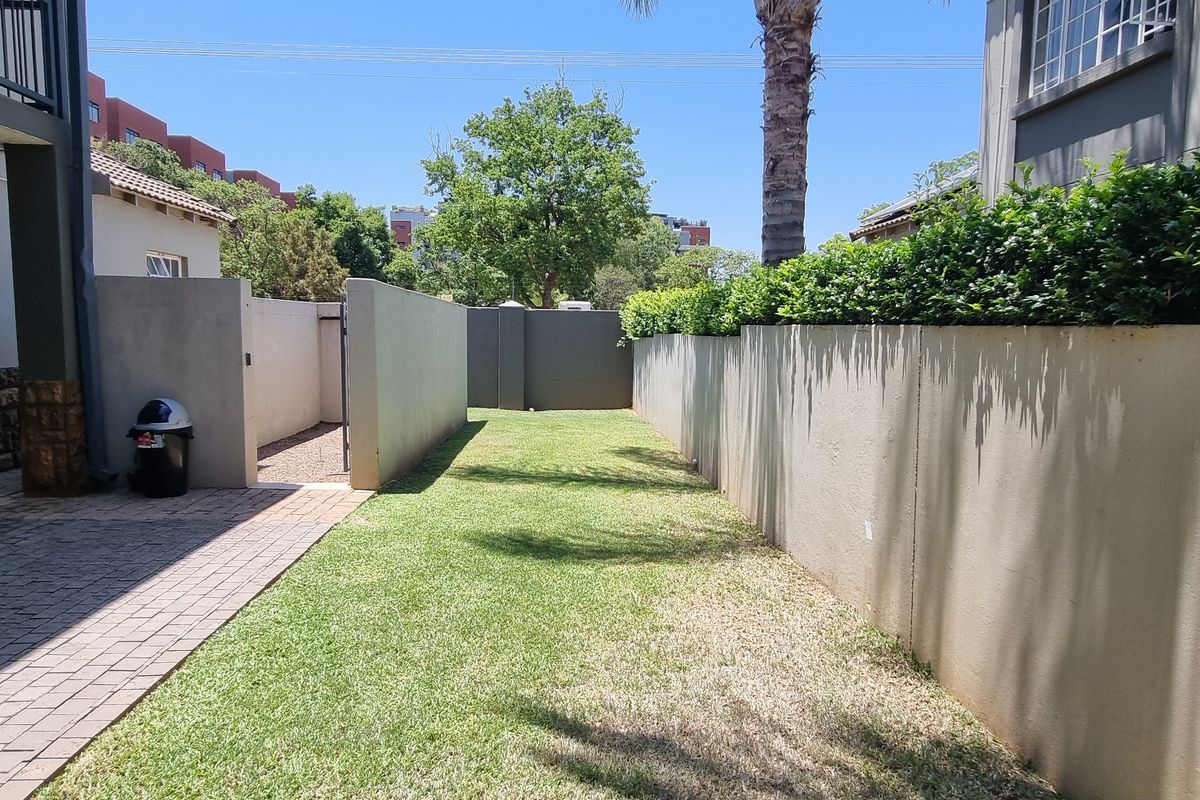 A private rear garden area featuring a paved patio, lawn, and high boundary walls, providing a secure outdoor space for the flat.