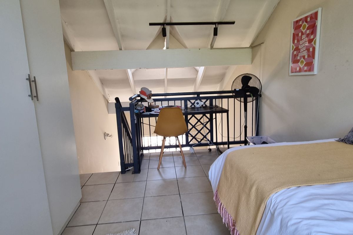 Loft-style bedroom featuring tiled flooring, exposed ceiling beams, and a metal balustrade overlooking the lower level, with built-in storage.