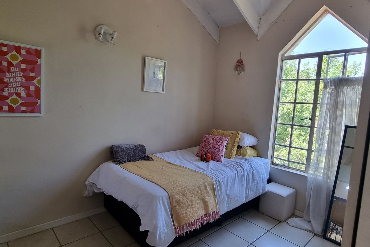 A bedroom featuring a vaulted ceiling, tiled flooring, and a large window that provides ample natural light.