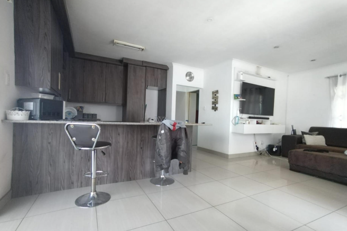 Open-plan living area featuring a modern kitchen with dark wood cabinetry, stone breakfast bar, and tiled flooring, seamlessly flowing into the lounge space.
