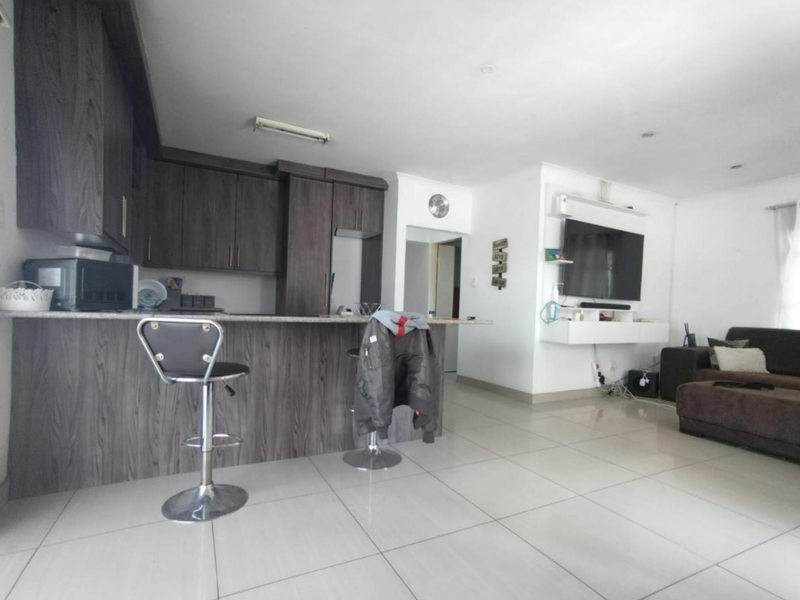 Open-plan living area featuring a modern kitchen with dark wood cabinetry, stone breakfast bar, and tiled flooring, seamlessly flowing into the lounge space.
