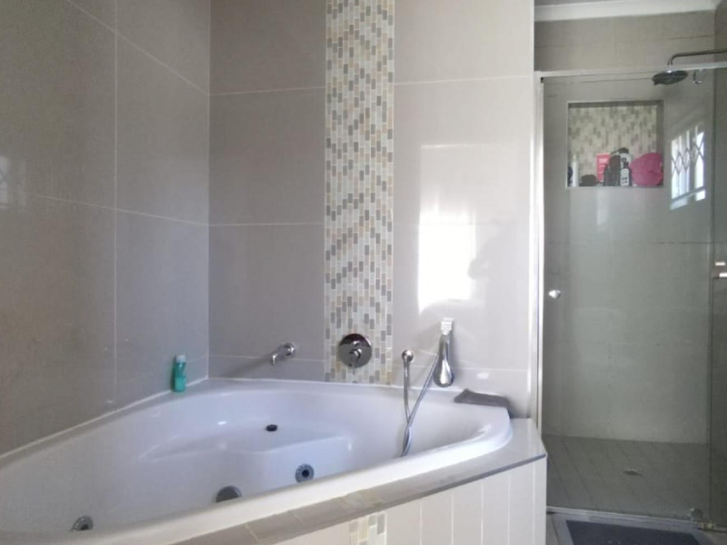 Modern bathroom featuring a corner spa bath with mosaic tile accents and a separate glass-enclosed shower with a built-in niche.