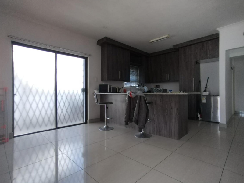 Open-plan kitchen featuring dark wood cabinetry, granite countertops, and a breakfast bar, with direct access to an outdoor area through a sliding glass door.