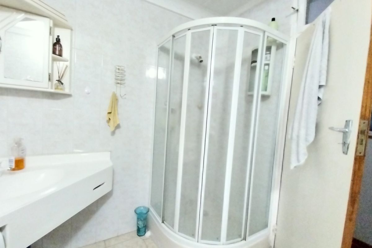 A functional bathroom featuring a corner shower enclosure, a wall-mounted vanity basin, and tiled wall finishes.