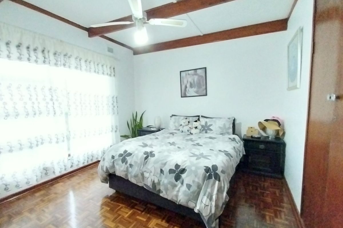 A bedroom featuring parquet flooring, exposed timber ceiling beams, a ceiling fan, and large windows allowing for natural light.