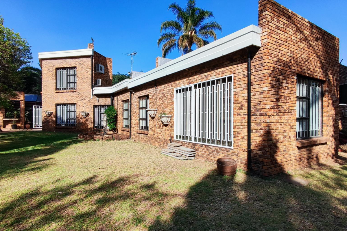 Rear view of a face brick house featuring a spacious garden, security bars on windows, and a built-in outdoor braai area.