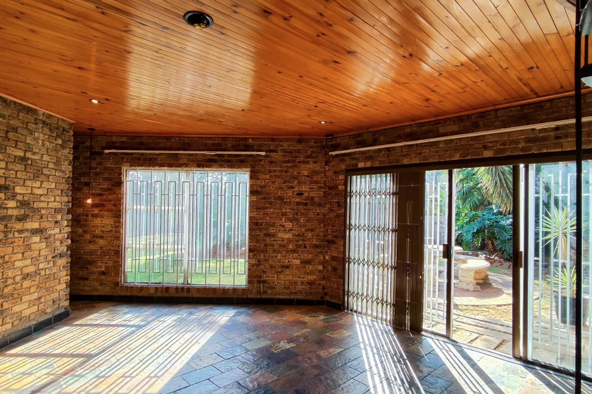 Spacious living area featuring exposed brick walls, a warm timber ceiling, slate flooring, and large sliding doors providing direct access to the garden.