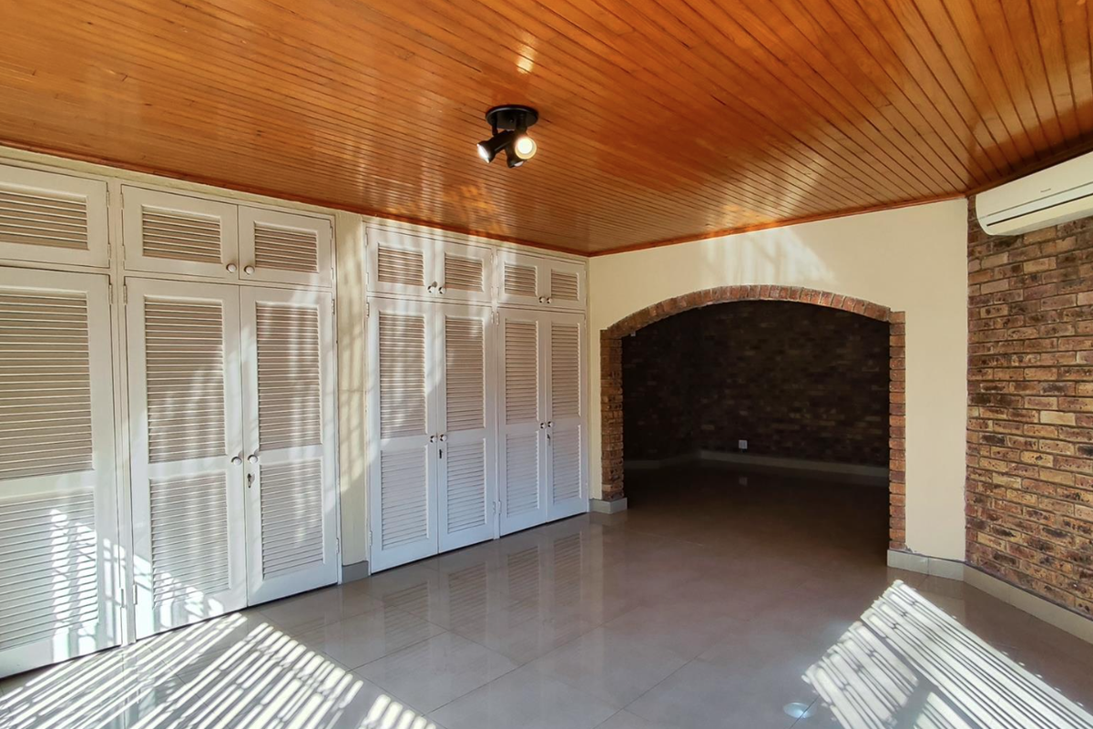 Spacious bedroom featuring extensive built-in cupboards, a warm timber ceiling, a rustic brick feature wall, and a split-system air conditioner.
