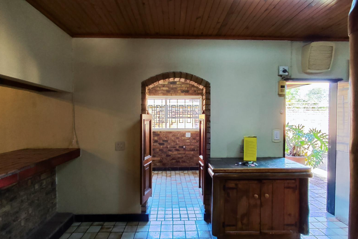A rustic kitchen area featuring a brick archway, timber ceiling, and tiled flooring, offering a functional layout with built-in brick and timber cabinetry.