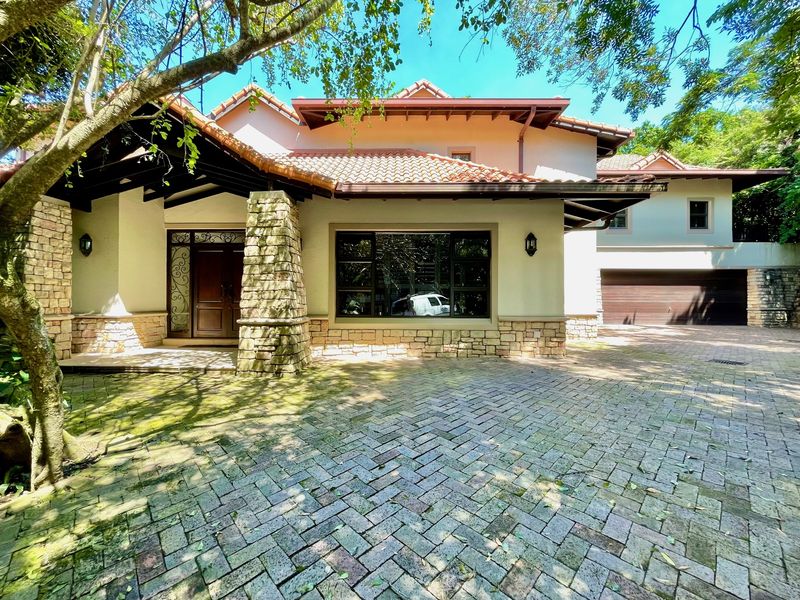 Front elevation of a multi-level residence featuring stone cladding, terracotta roof tiles, a paved driveway, and an integrated double garage.