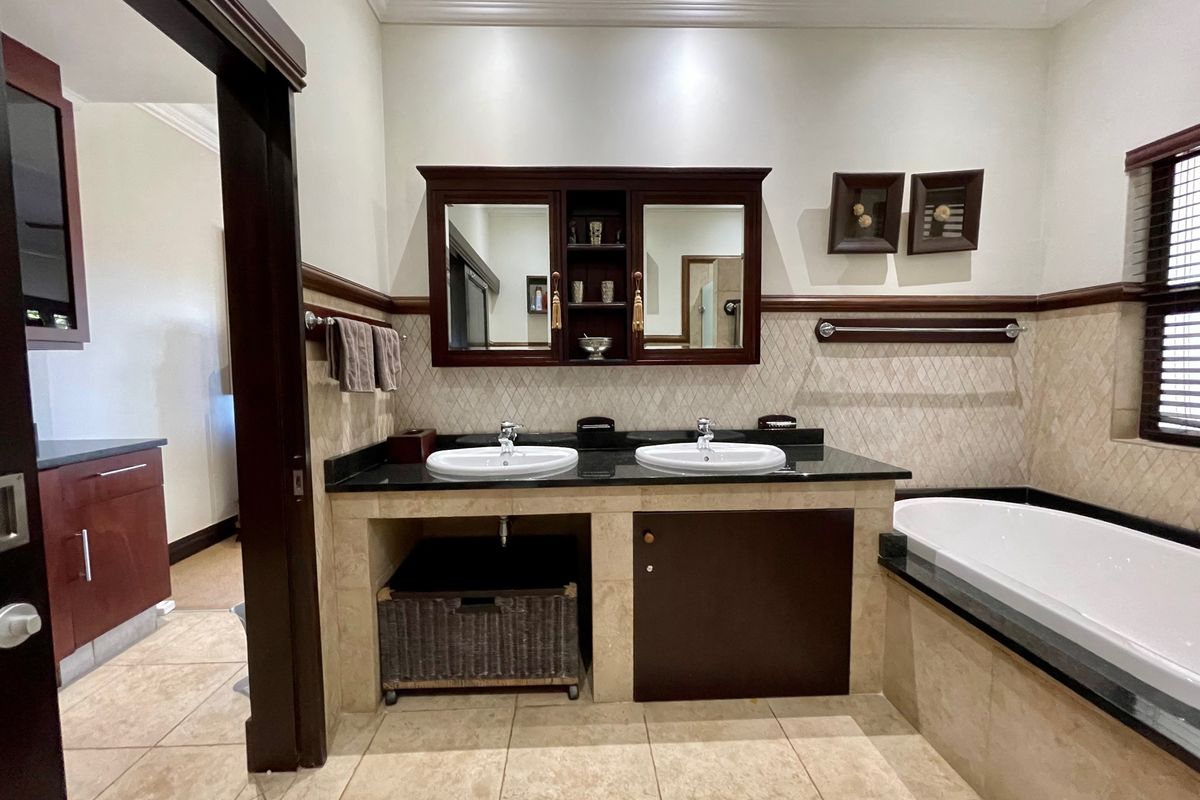A well-appointed bathroom featuring a double vanity with stone countertops, a built-in medicine cabinet, and a spacious drop-in bathtub with tiled surrounds.