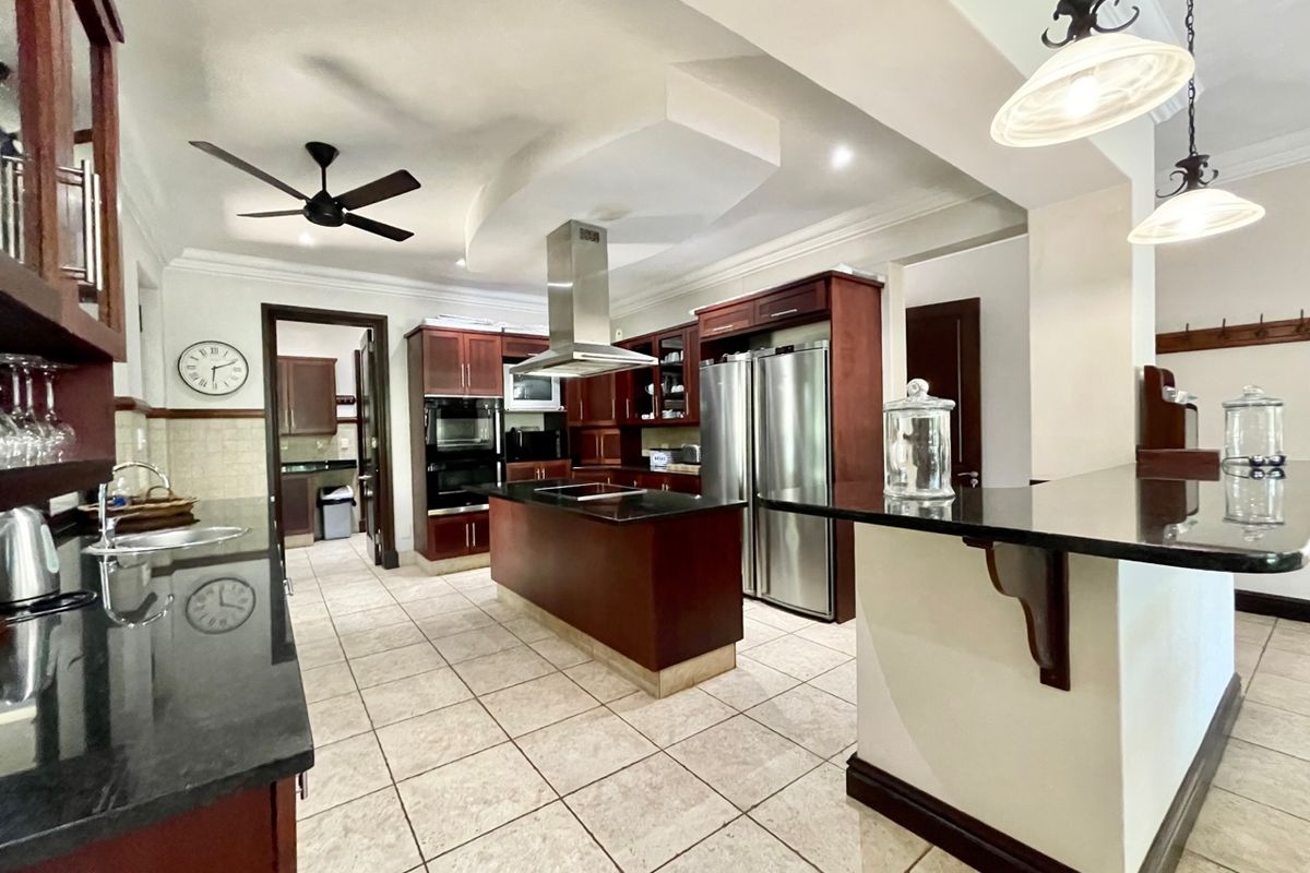 Spacious kitchen featuring dark wood cabinetry, granite countertops, a central island with a cooktop, and stainless steel appliances.