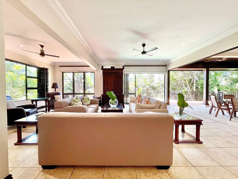 Spacious open-plan living area featuring tiled floors, ceiling fans, and large sliding glass doors that open onto a covered patio with garden views.