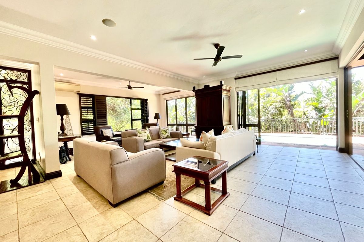 Spacious open-plan living area featuring large sliding glass doors, tiled flooring, ceiling fans, and recessed lighting, offering seamless access to the outdoor balcony.