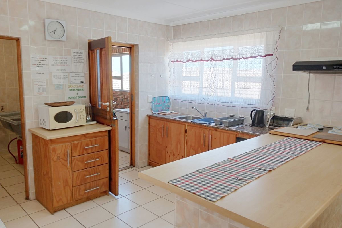 A functional kitchen featuring wooden cabinetry, tiled splashbacks, a breakfast counter, and direct access to an adjacent utility area.