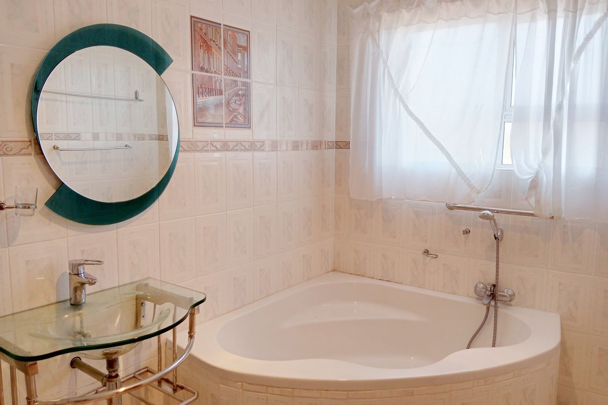 A functional bathroom featuring a corner bathtub, glass vessel sink, and tiled finishes, offering a clean and practical space.