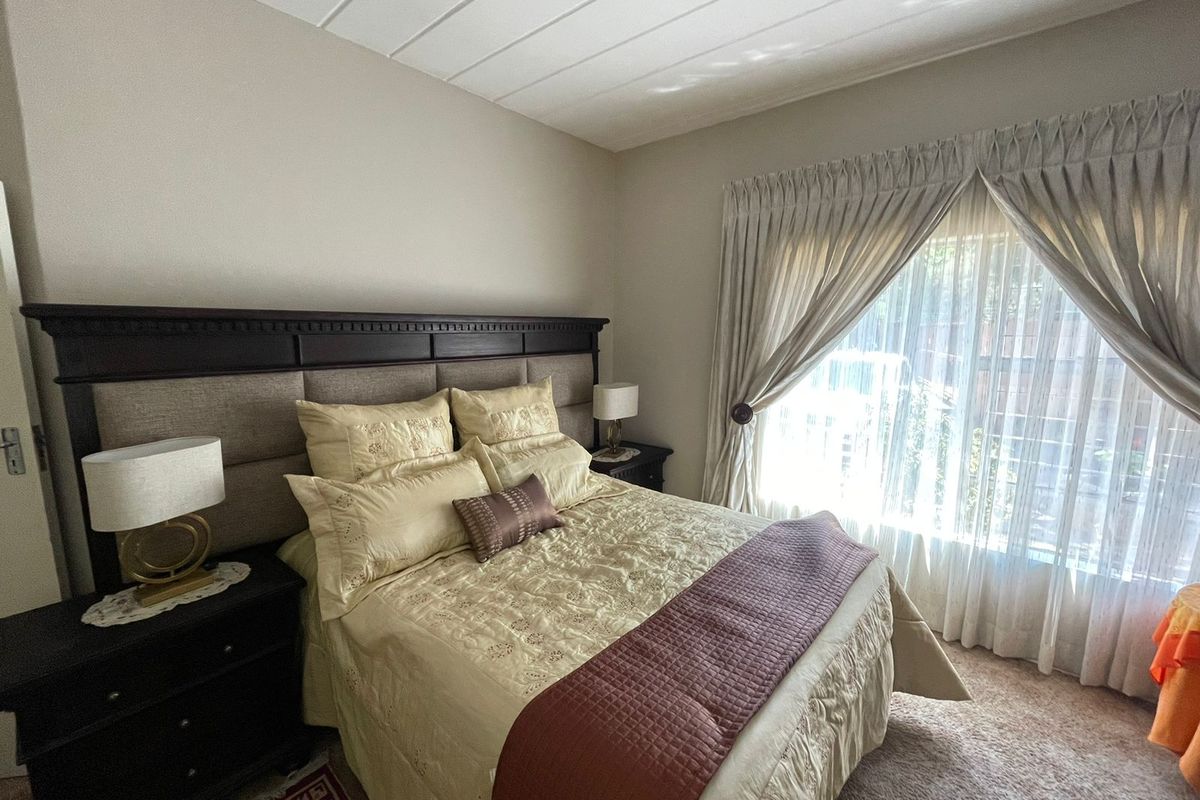 A well-maintained bedroom featuring carpeted flooring, a panelled ceiling, and large windows with installed curtain tracks for natural light.