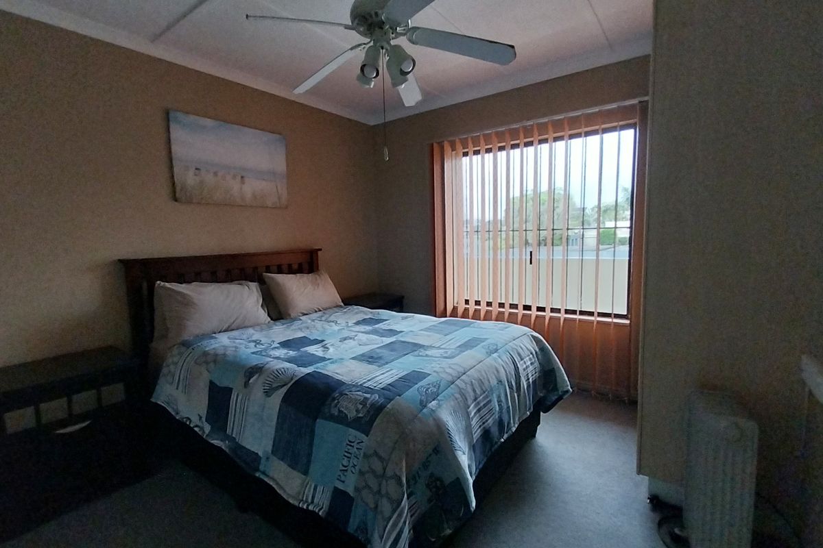 A standard bedroom featuring a ceiling fan and vertical window blinds, offering a functional space with neutral wall tones.