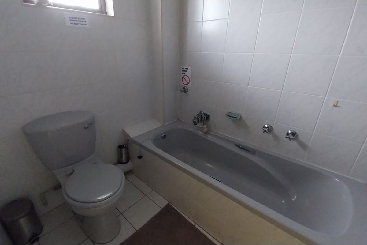 A functional bathroom featuring a built-in bathtub, toilet, and neutral wall and floor tiling.