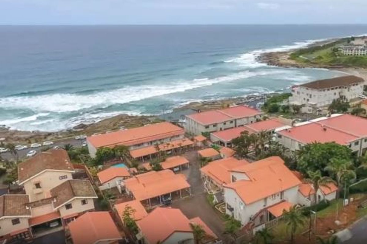 Aerial view of a coastal apartment complex featuring multiple buildings with terracotta-style roofs, situated near the ocean shoreline.