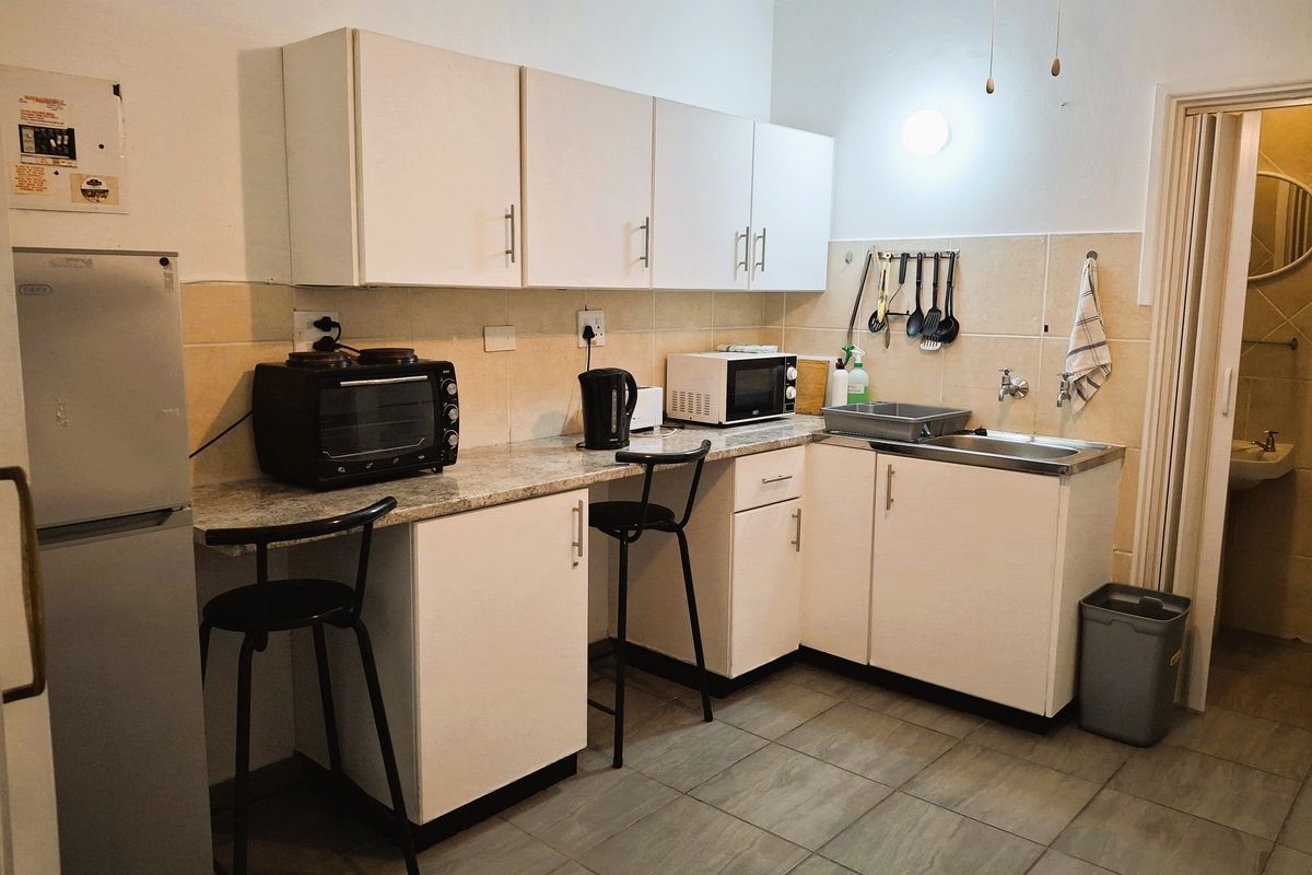 A functional kitchen featuring white cabinetry, stone-look countertops, a stainless steel sink, and tiled flooring, providing a practical workspace for daily meal preparation.