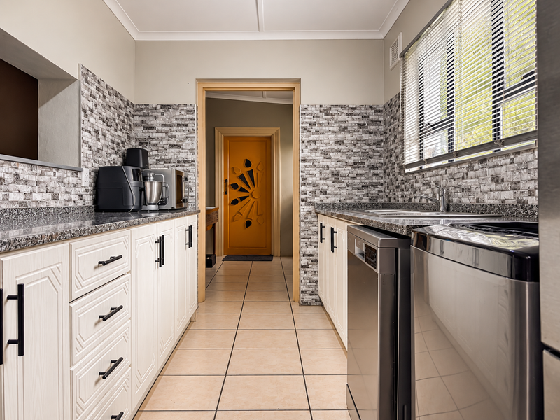 A functional kitchen featuring stone-look countertops, tiled backsplash, ample cabinetry, and ceramic floor tiles, leading through to an interior doorway.