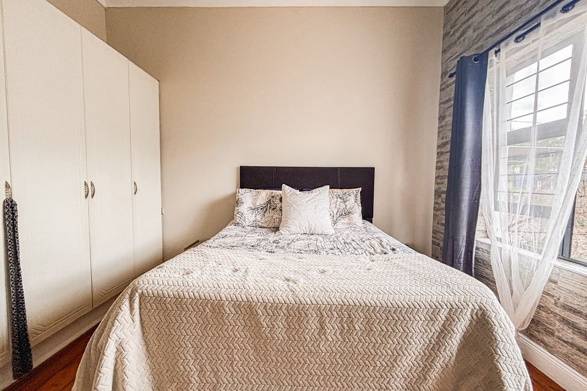 A well-maintained bedroom featuring built-in cupboards, warm wooden flooring, and a decorative feature wall with natural light.