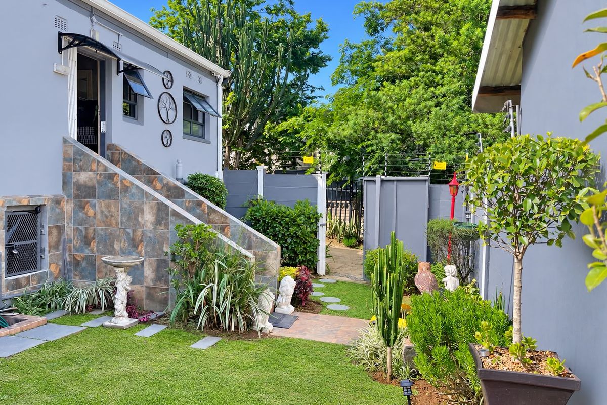 A well-maintained rear garden area featuring a tiled staircase leading to an entrance, surrounded by established landscaping and secure boundary walls.