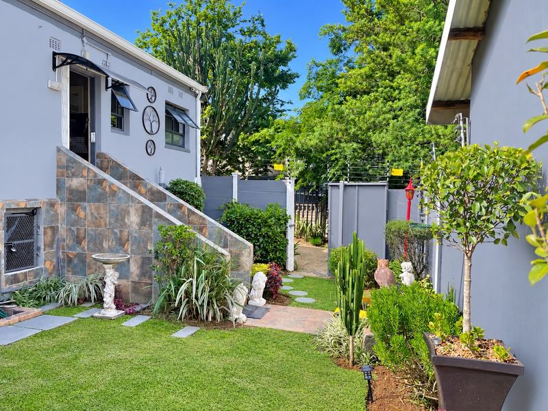 A well-maintained rear garden area featuring a tiled staircase leading to an entrance, surrounded by established landscaping and secure boundary walls.