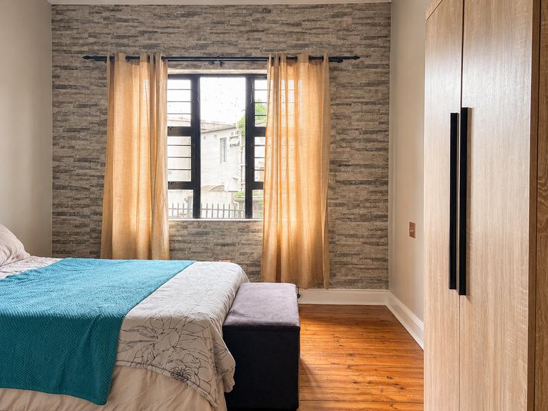 A well-maintained bedroom featuring polished timber flooring, a built-in wardrobe, and a textured feature wall with security-fitted windows.