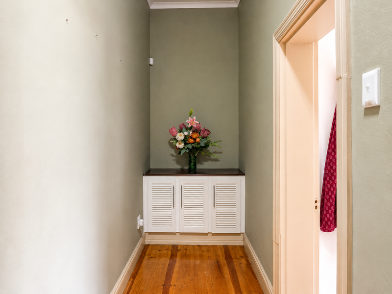 A hallway featuring polished timber flooring, built-in cabinetry, and neutral wall tones, providing a functional transition space within the townhouse.