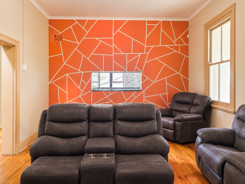 A living room featuring polished timber flooring, a sash window, and a distinctive geometric feature wall.