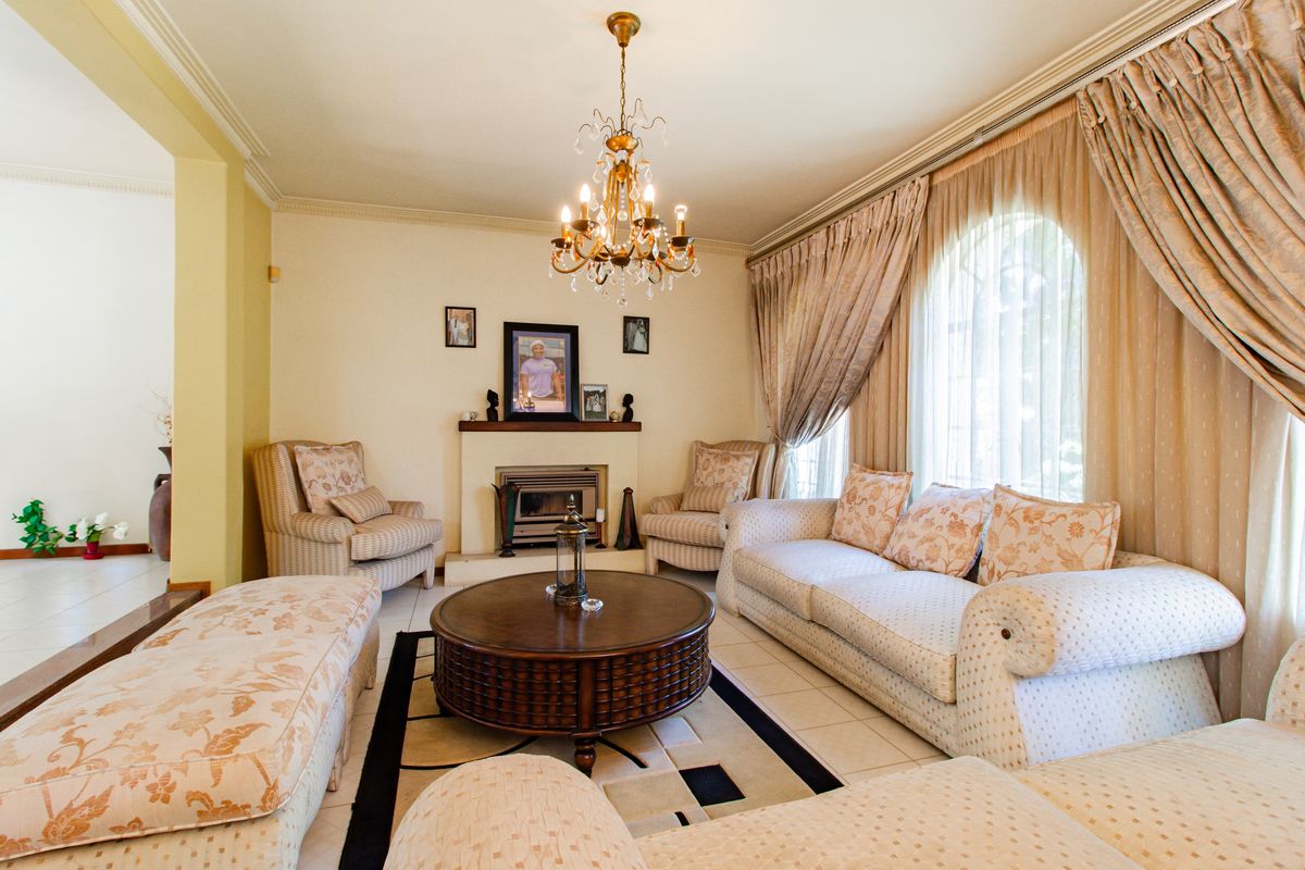 A comfortable living room featuring a fireplace, elegant chandelier, arched windows, and tiled flooring, offering a warm and inviting atmosphere.