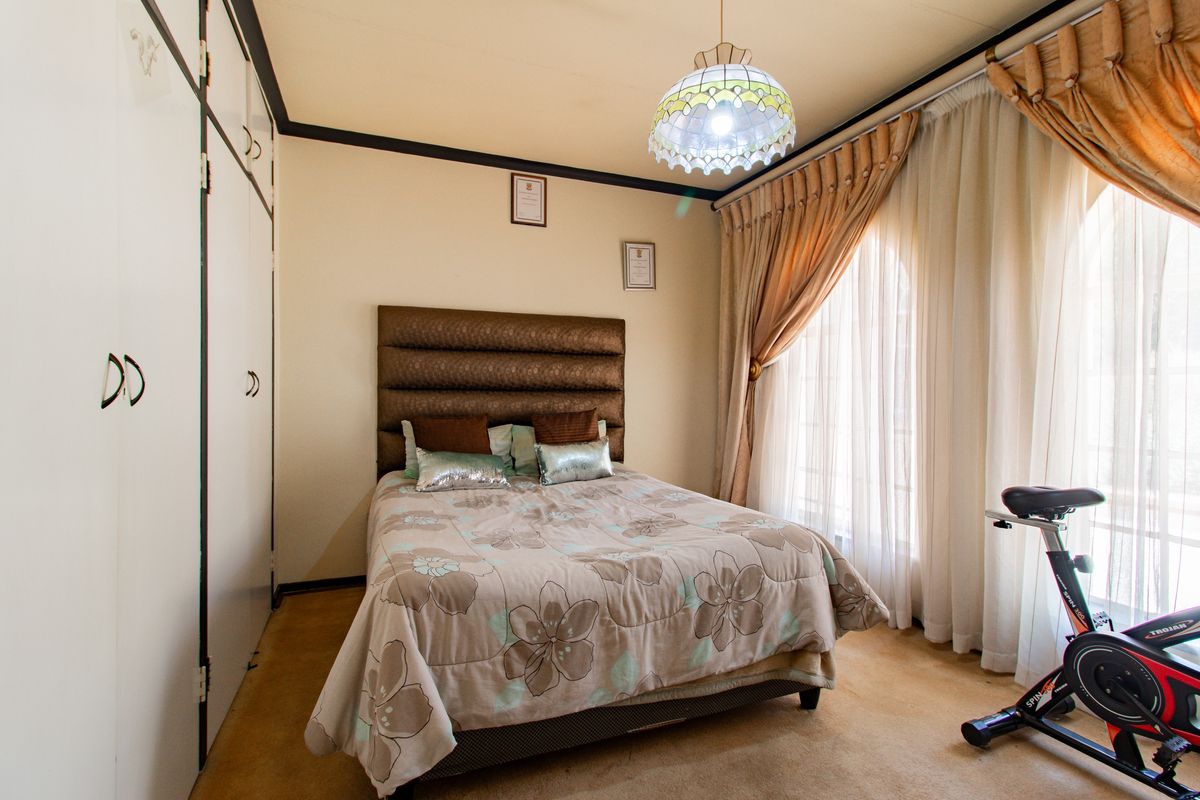 A bedroom featuring built-in cupboards, carpeted flooring, and large windows with curtain rails, providing natural light.