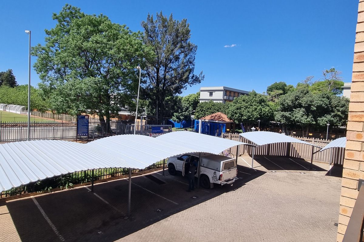 An elevated view of a paved parking area featuring multiple covered carports and brick boundary walls.