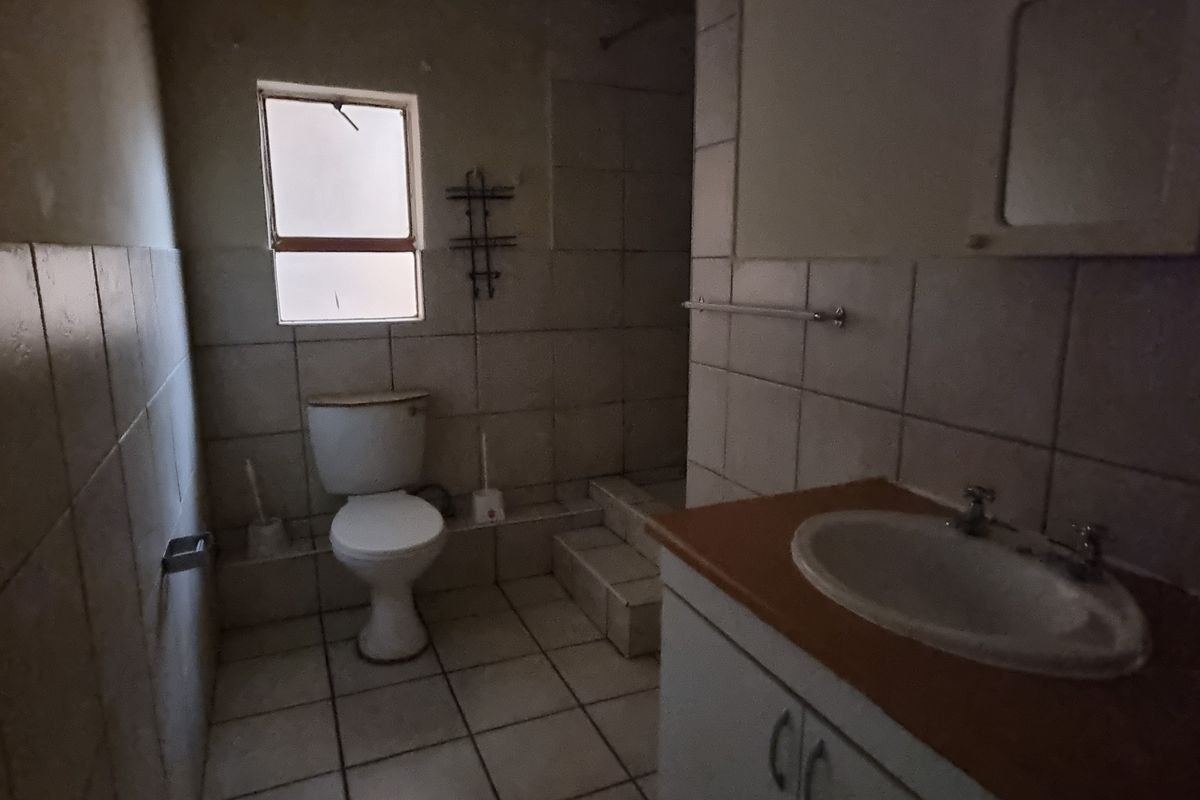 A dated bathroom featuring a vanity cabinet, washbasin, toilet, and tiled finishes, requiring modernization to improve its overall appeal and functionality.