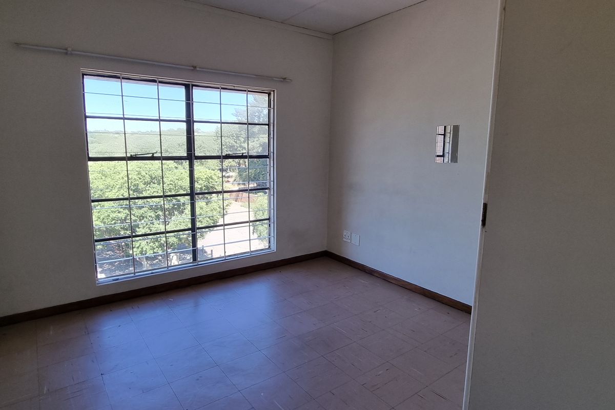 An empty bedroom featuring tiled flooring, a large window with security bars, and neutral wall finishes, offering a blank canvas for potential updates.