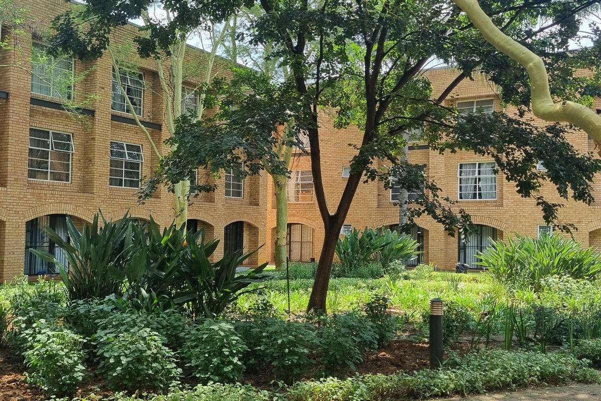 A view of the rear facade of a face brick apartment complex featuring established garden landscaping and mature trees.