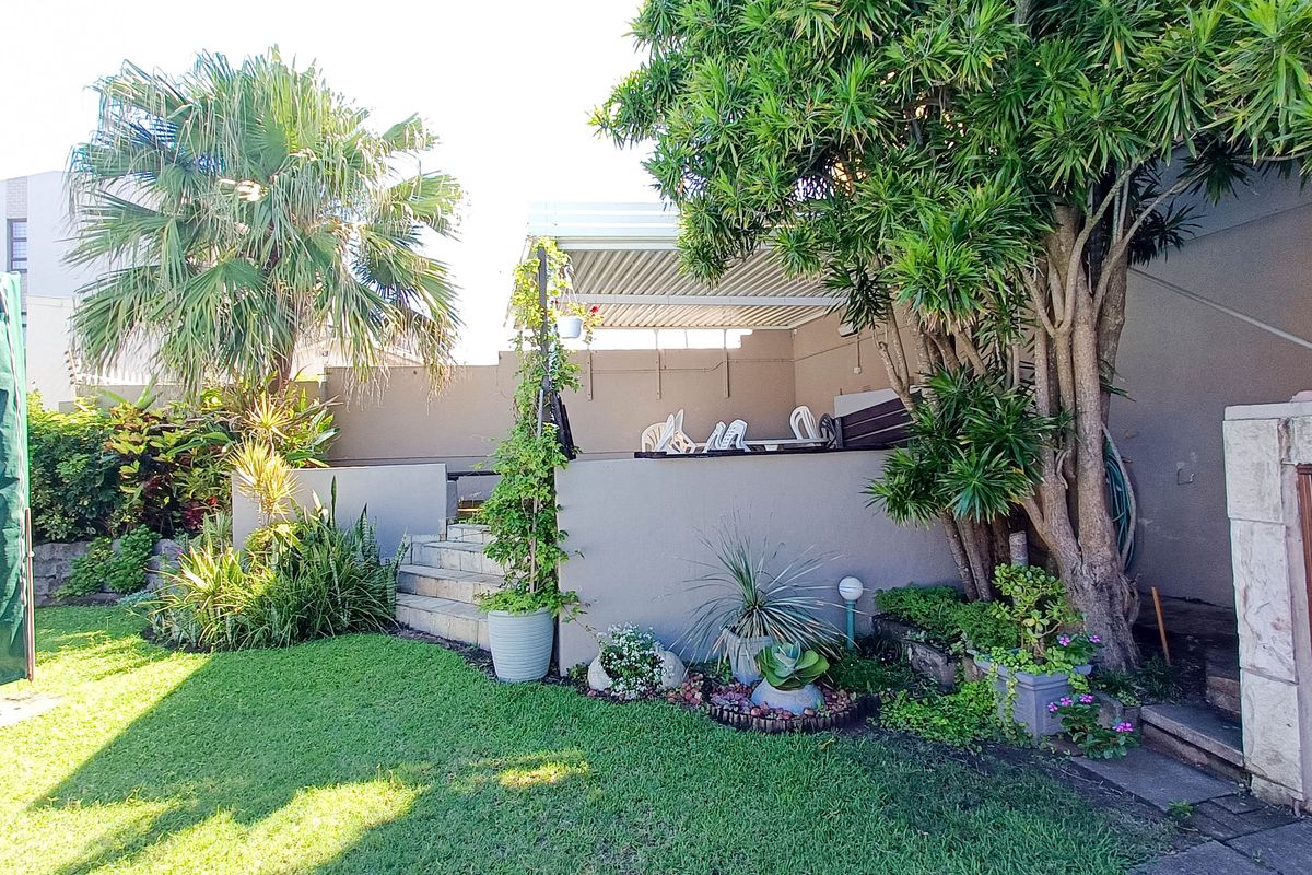 A private rear garden area featuring a paved patio with a pergola, landscaped lawn, and established trees.