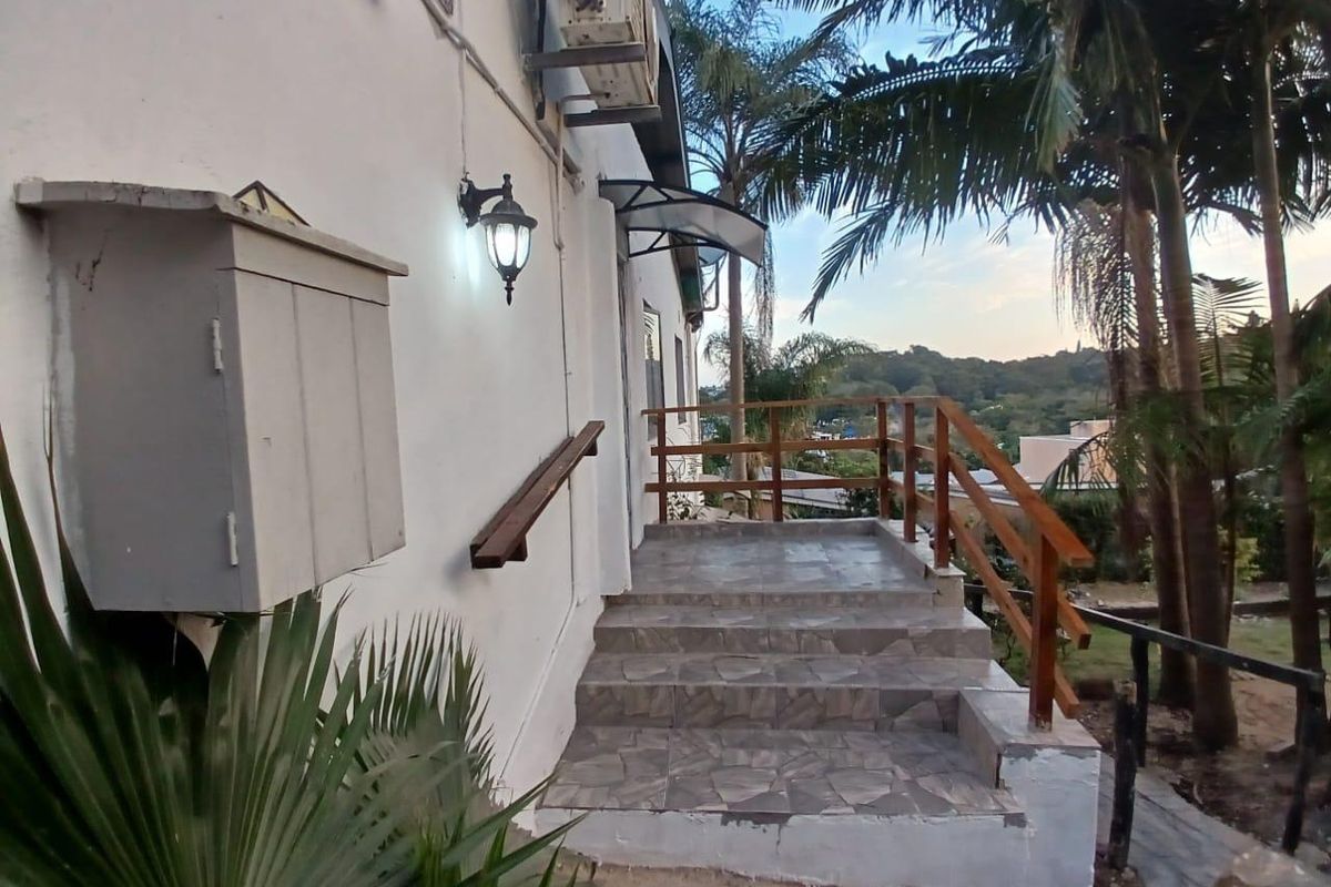 Exterior rear staircase with tiled steps, wooden handrails, and wall-mounted lighting, leading to an elevated outdoor area.