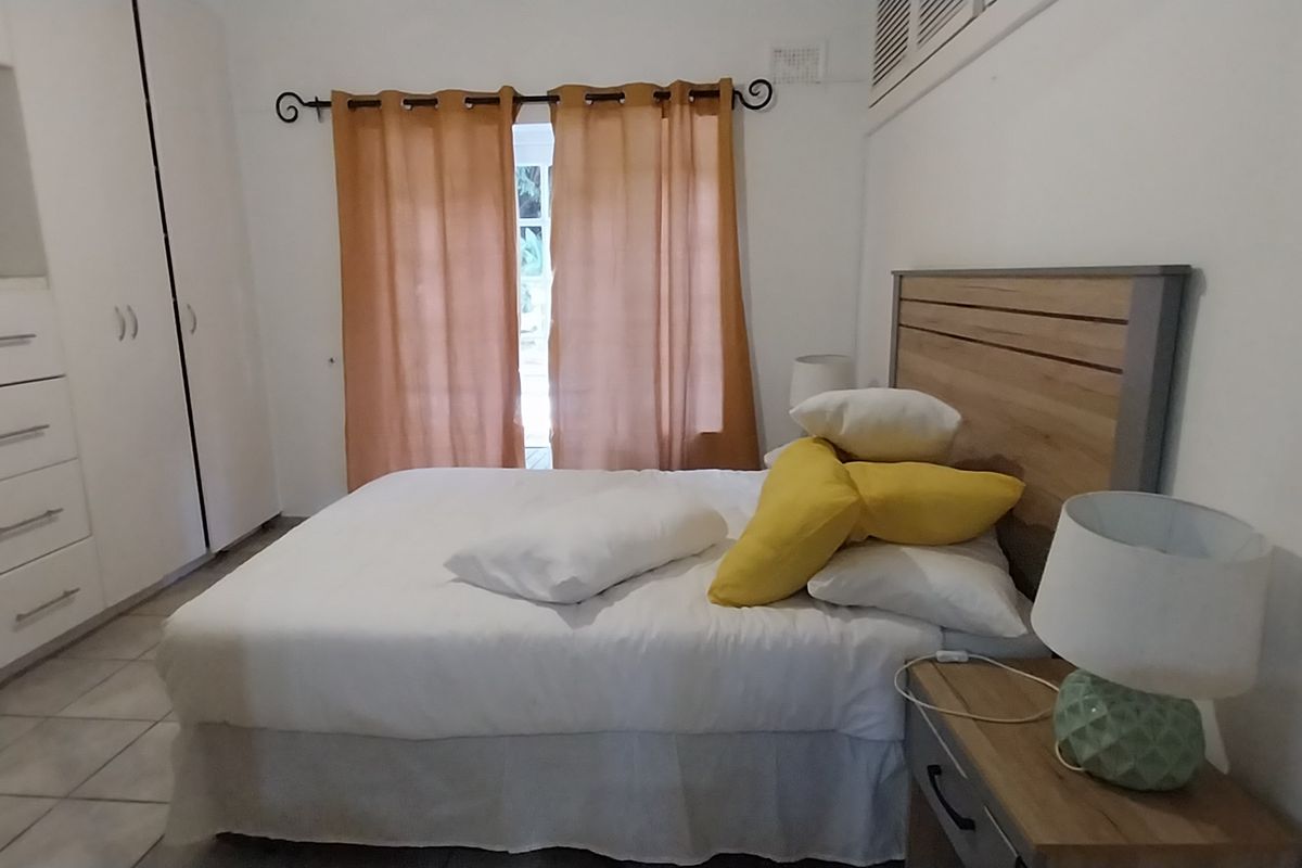 A functional bedroom featuring built-in cupboards, tiled flooring, and direct access to an outdoor area through a glass door.