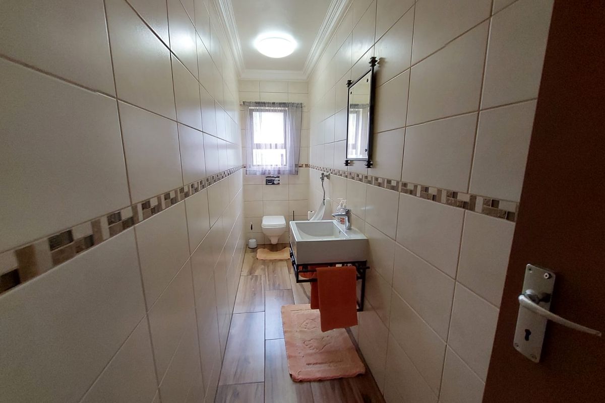 A narrow, well-maintained bathroom featuring full-height wall tiling, a wall-mounted basin, and wood-look floor tiles.