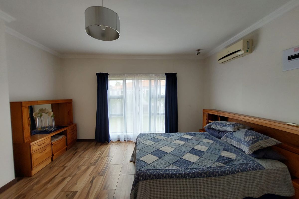 A spacious bedroom featuring wood-look laminate flooring, a wall-mounted air conditioning unit, and a built-in wooden headboard.