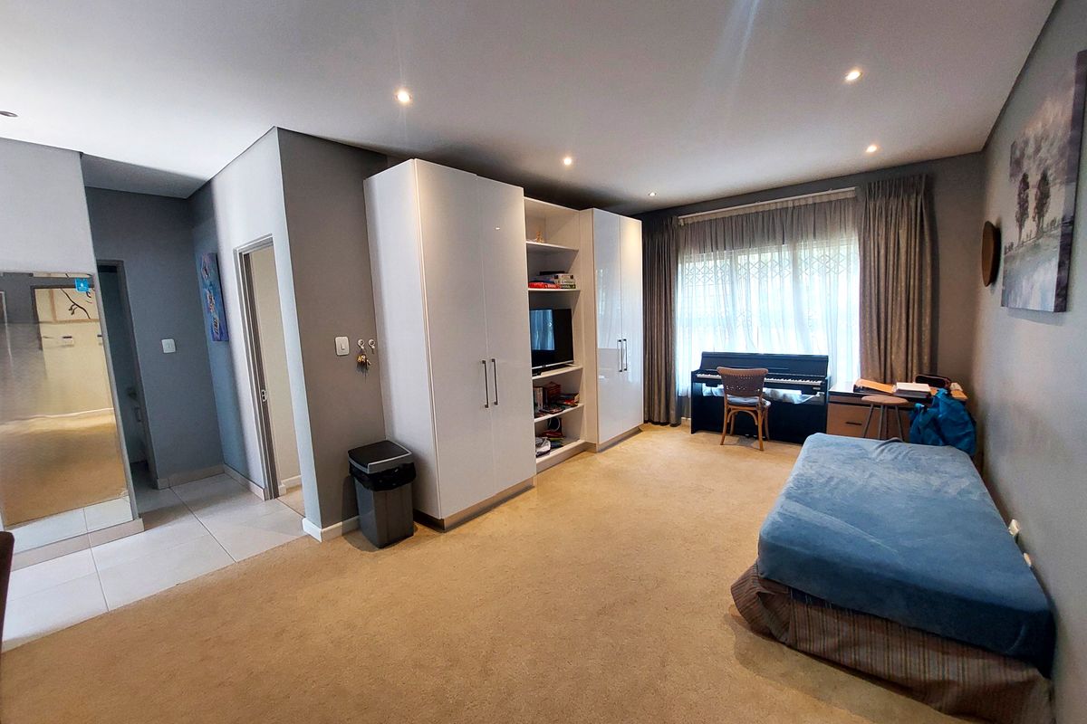 Spacious bedroom featuring neutral wall tones, built-in cupboards, recessed downlighting, and large windows with security gates.